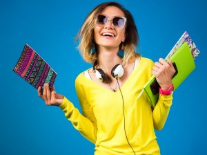 beautiful young hipster woman, smiling, happy, emotional, in yellow shirt, blue background, headphones, student, fashion blogger, holding books, smartphone, sunglasses, summer style, positive emotion