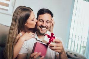 Woman surprising his boyfriend with a gift on the couch at home