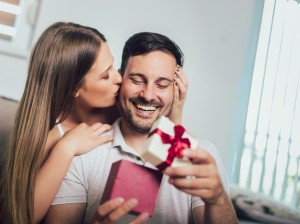 Woman surprising his boyfriend with a gift on the couch at home