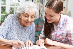 Teenage Granddaughter Helping Grandmother With Crossword Puzzle